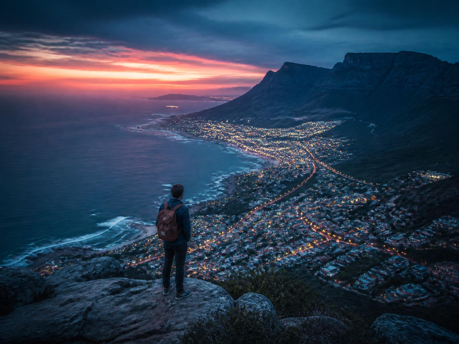 Traveler with a backpack looking over a coastal city at dusk